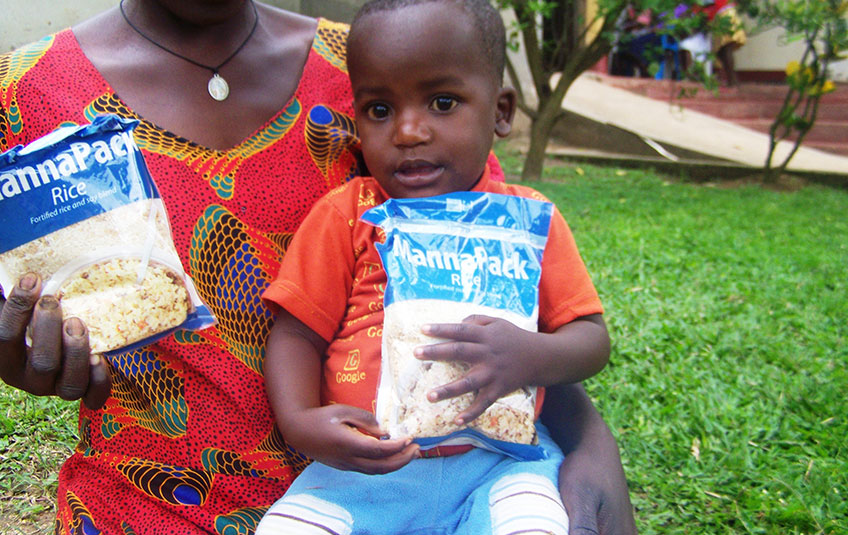A Ugandan mother holds her son and both hold FMSC MannaPack bags