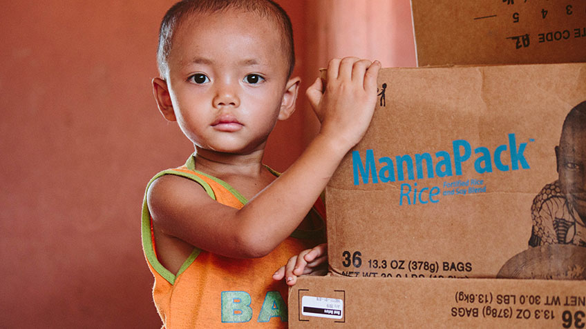 a young child standing beside a box of FMSC's MannaPack meals