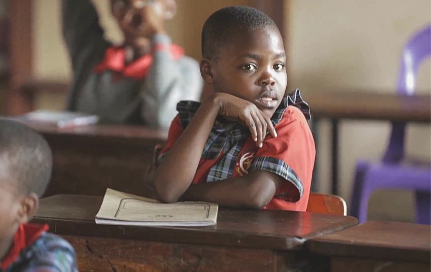 young girl in school uniform at desk with schoolwork