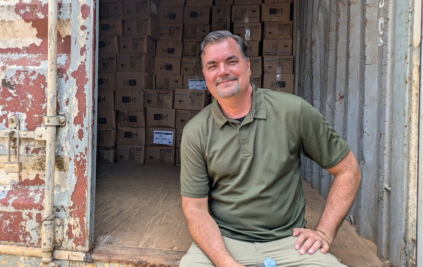 FMSC JJ Slag smiling with shipping container of FMSC boxes of food