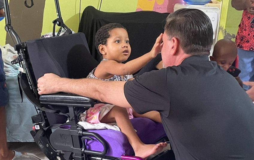 FMSC CEO JJ Slag with young girl from Dominican Republic in wheelchair touching his face.