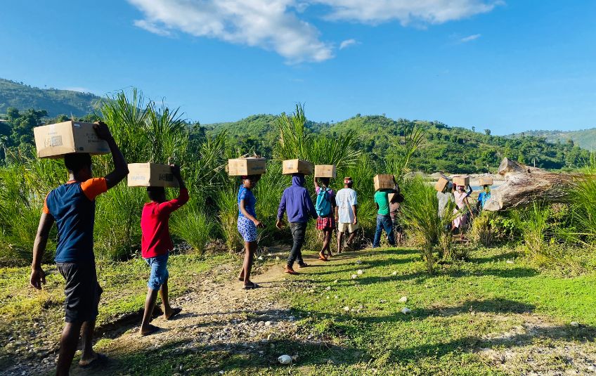 men carrying FMSC food boxes on their heads down path
