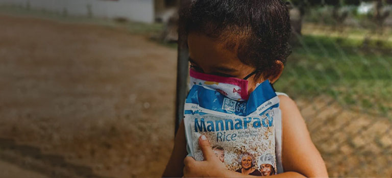 a masked Venezuelan girl clutches a bag of FMSC food