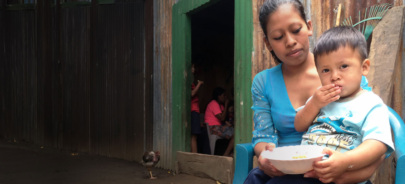 A mother holds a young child eating FMSC food